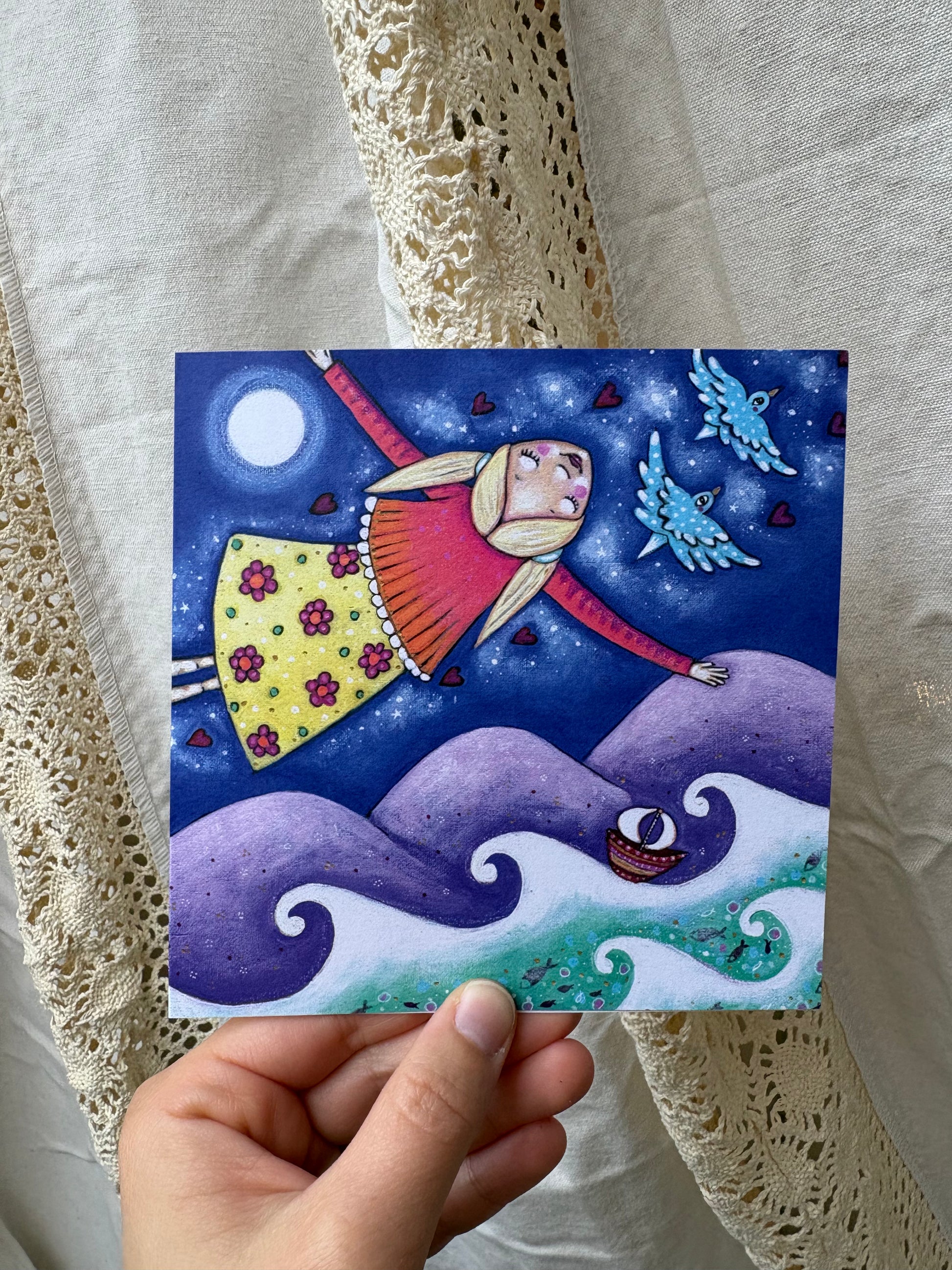 Home greeting card: hand-painted illustration of a blonde girl flying above the ocean alongside two blue-birds and some hearts, the moon in the sky and a ship sailing the sea below. 