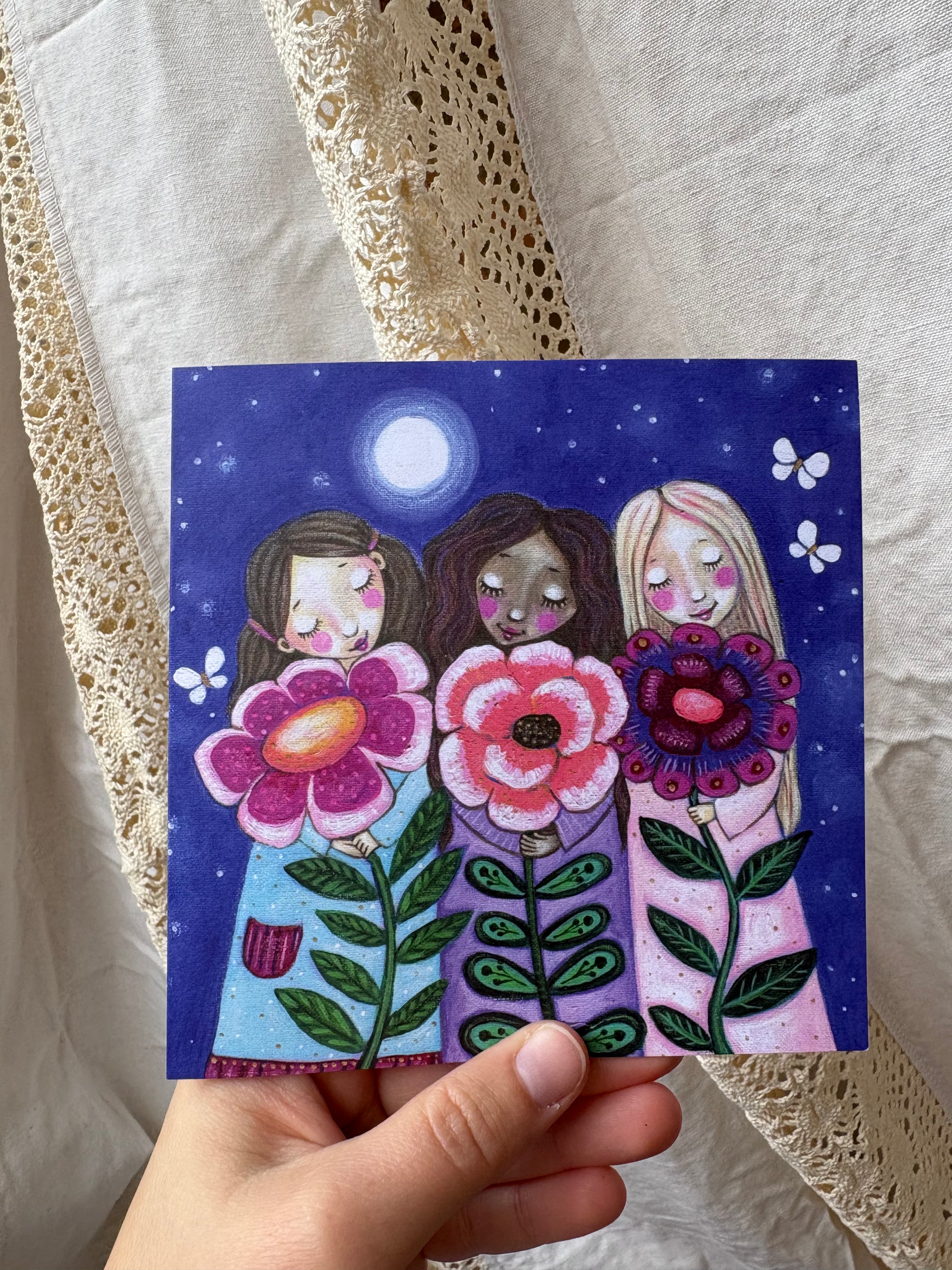 Grow greeting card: hand-painted illustration of three girls of different skin tones each holding a large flower under a starry moonlit sky, with butterflies, from What Makes Your Heart Sing