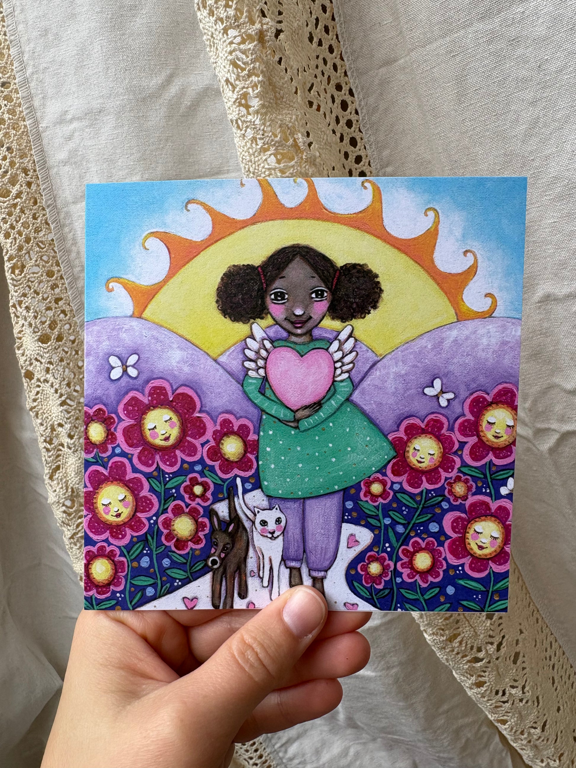 Love greeting card: hand-painted illustration of a girl holding a winged heart in a sunlit flower field, with a brown dog and a white cat, from What Makes Your Heart Sing