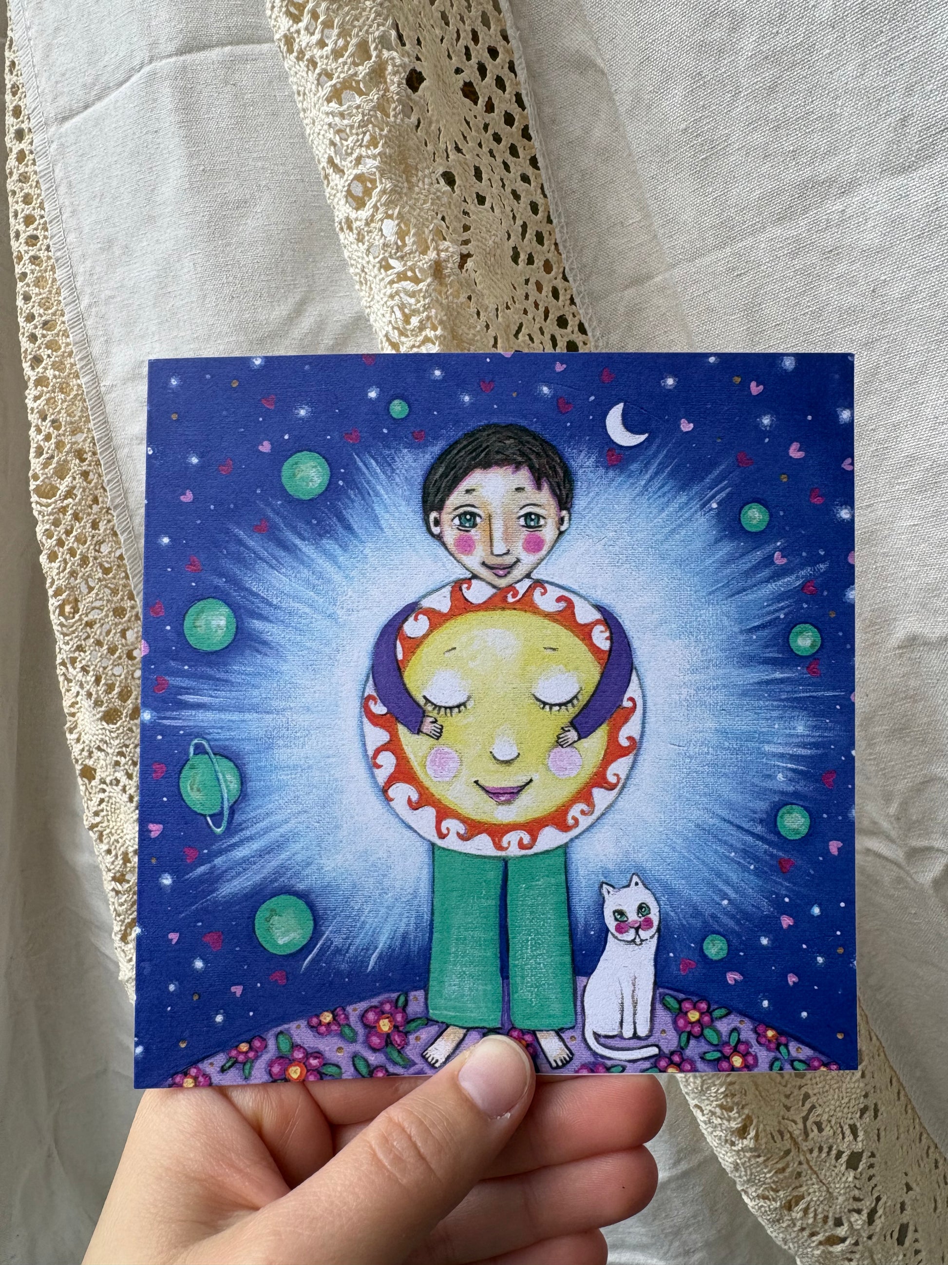 Shine greeting card: hand-painted illustration of a boy hugging a glowing sun against a starry night sky, with planets, a crescent moon and a white cat, from What Makes Your Heart Sing